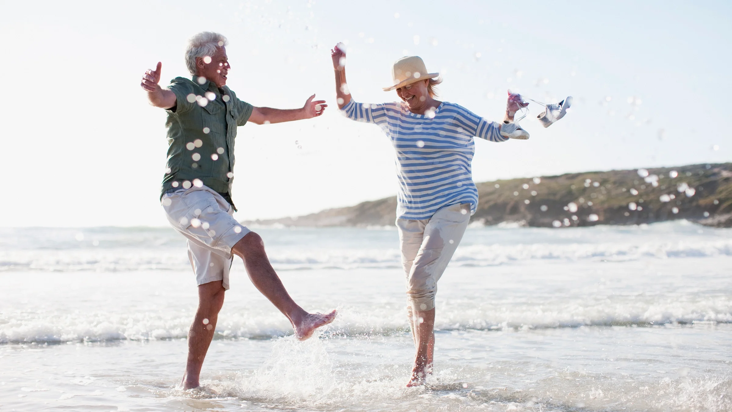 A retired couple kicks up water on the beach.