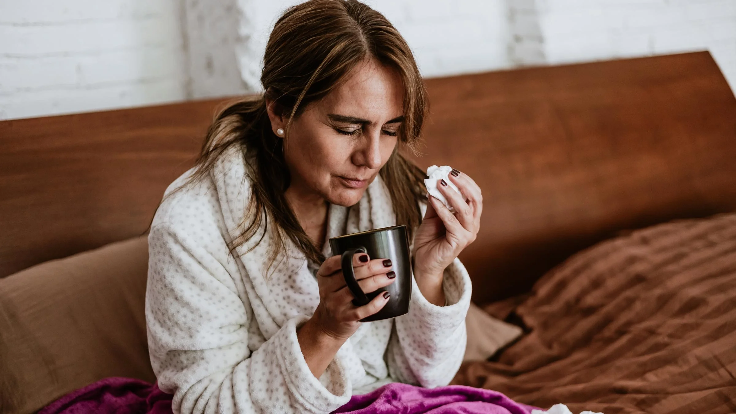 Woman sneezing and drinking tea while sick at home with the flu.