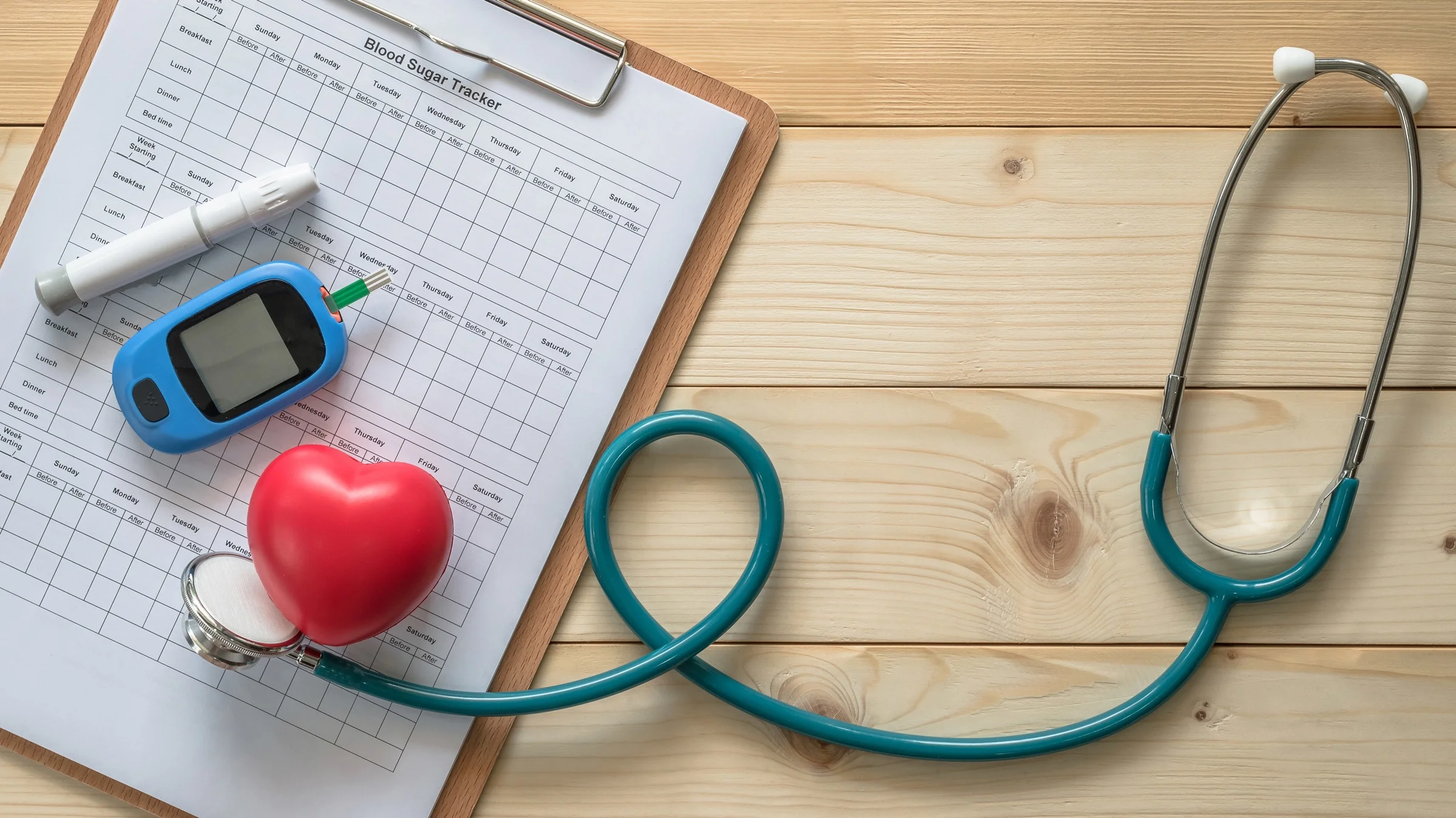 A blood examination kit, blood sugar tracker, heart, stethoscope, and blood sugar tracker on a desk.