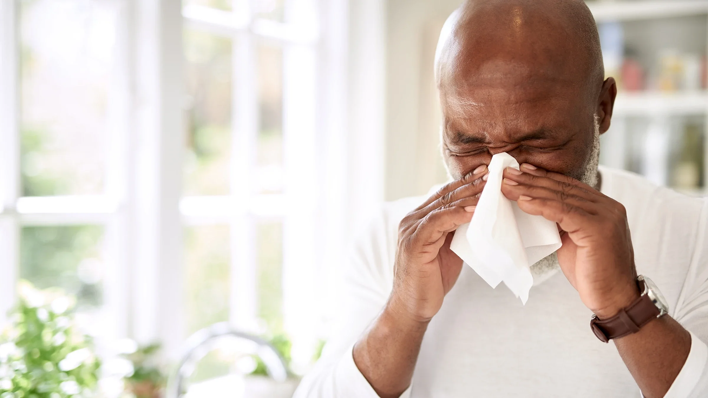 Man blowing his nose into a tissue.