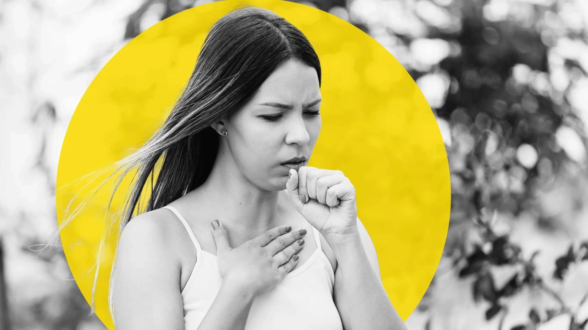 Black and white portrait of a young woman coughing. She had one hand on her upper chest and one hand in front of her mouth in a fist. There is a graphic yellow circle added behind her head.