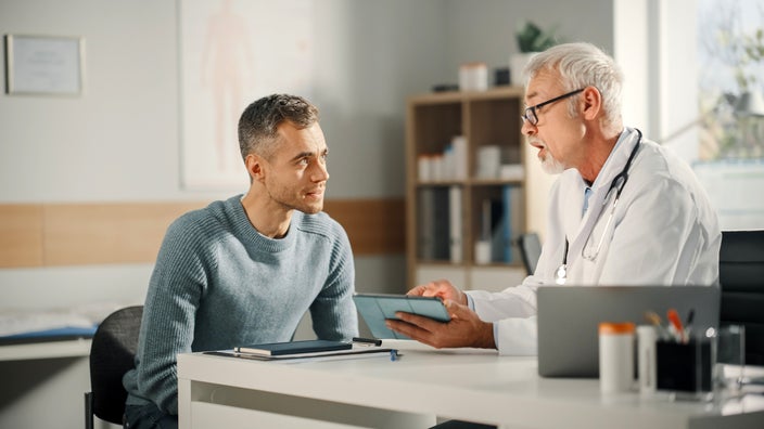A doctor sits at a desk talking to a patient.