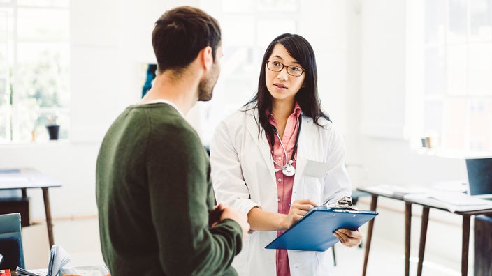 Healthcare professional talking to patient while holding clipboard.