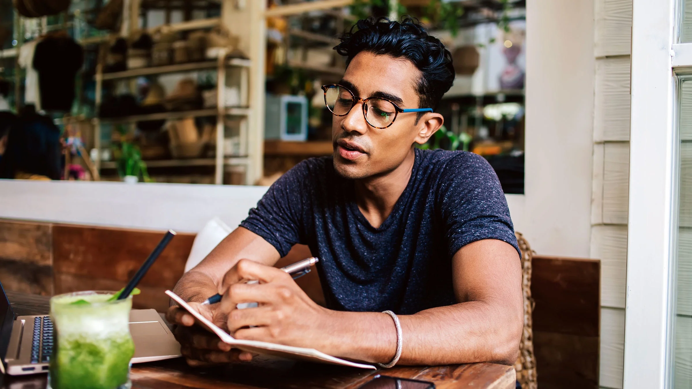 A man writes in a notebook while dining alone at a restaurant.