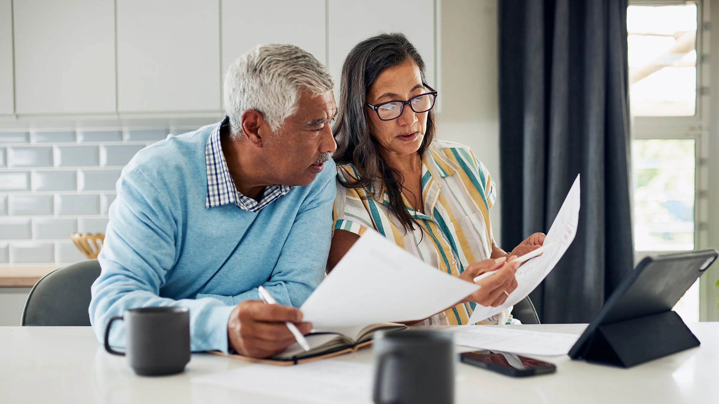 Couple is sitting at their kitchen table reviewing financial documents.