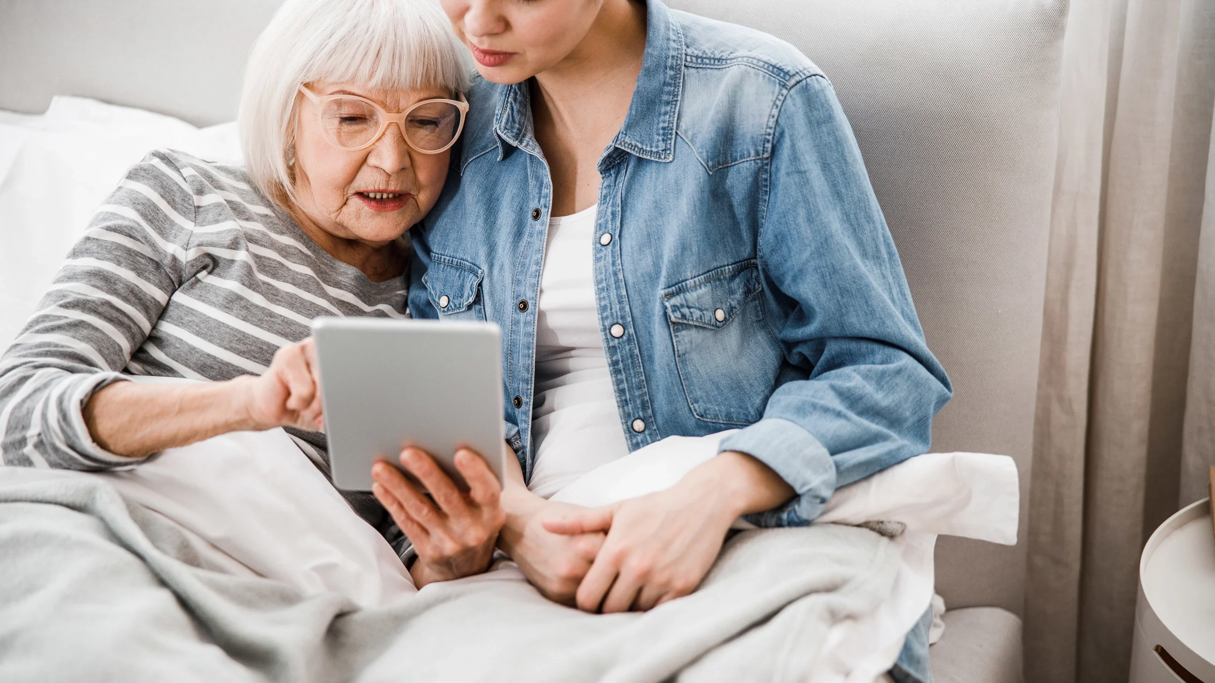 An older adult showing a tablet screen to their adult grandchild.