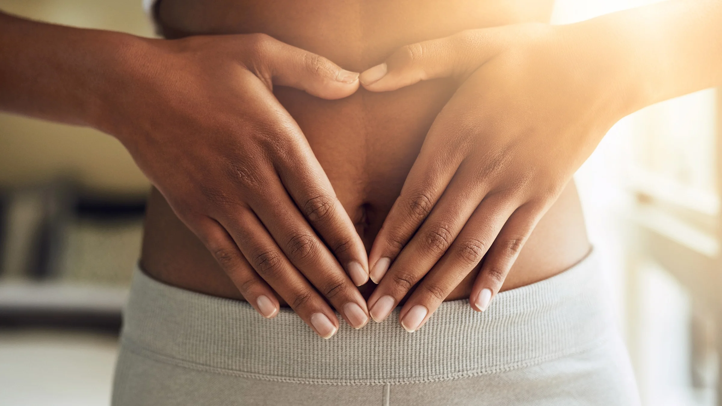 A close-up on a person's hands making a heart shape on their stomach.