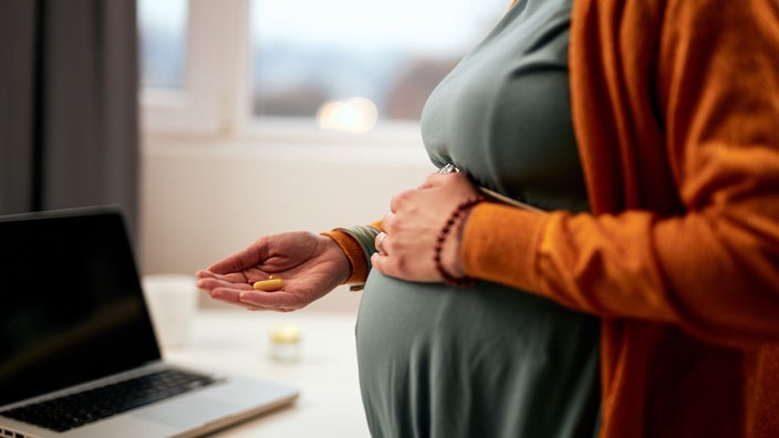 A cropped shot of a person's pregnant belly and their hand holding a pill.