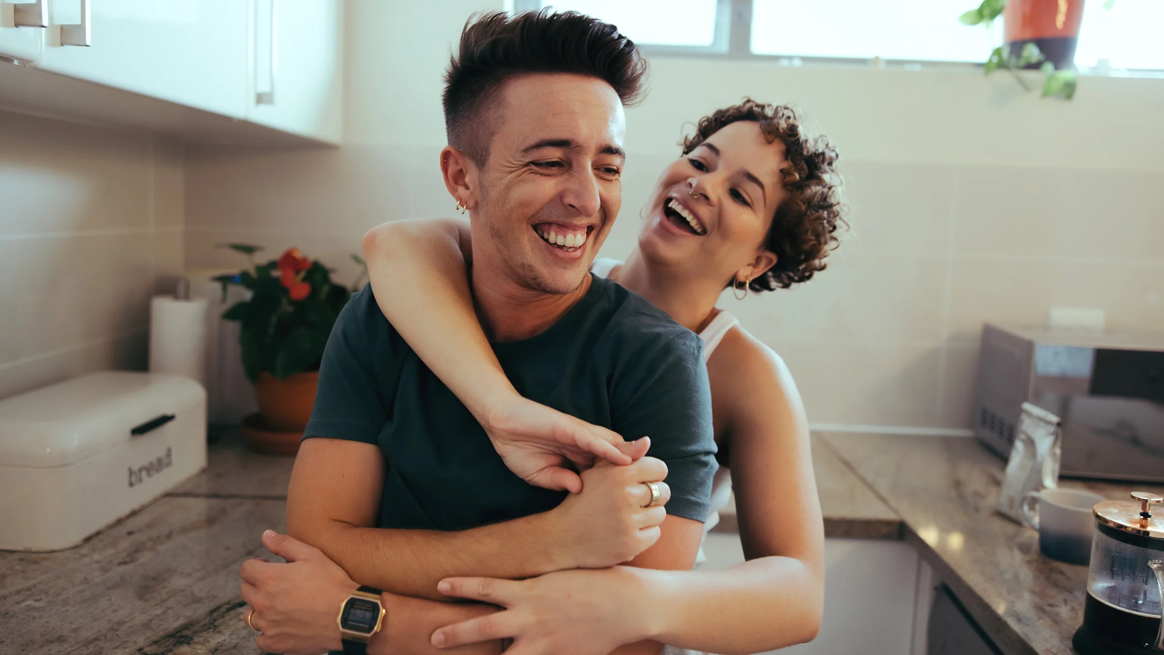 Queer couple hugging and smiling in their kitchen.