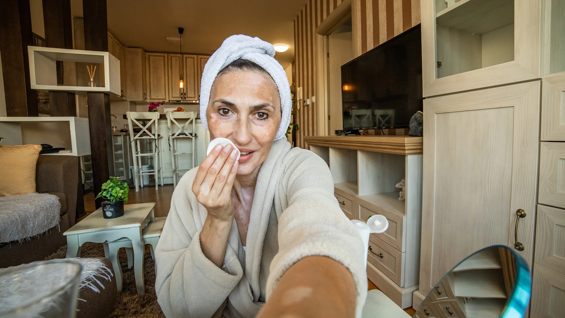 A woman applies toner to her face with a cotton round.