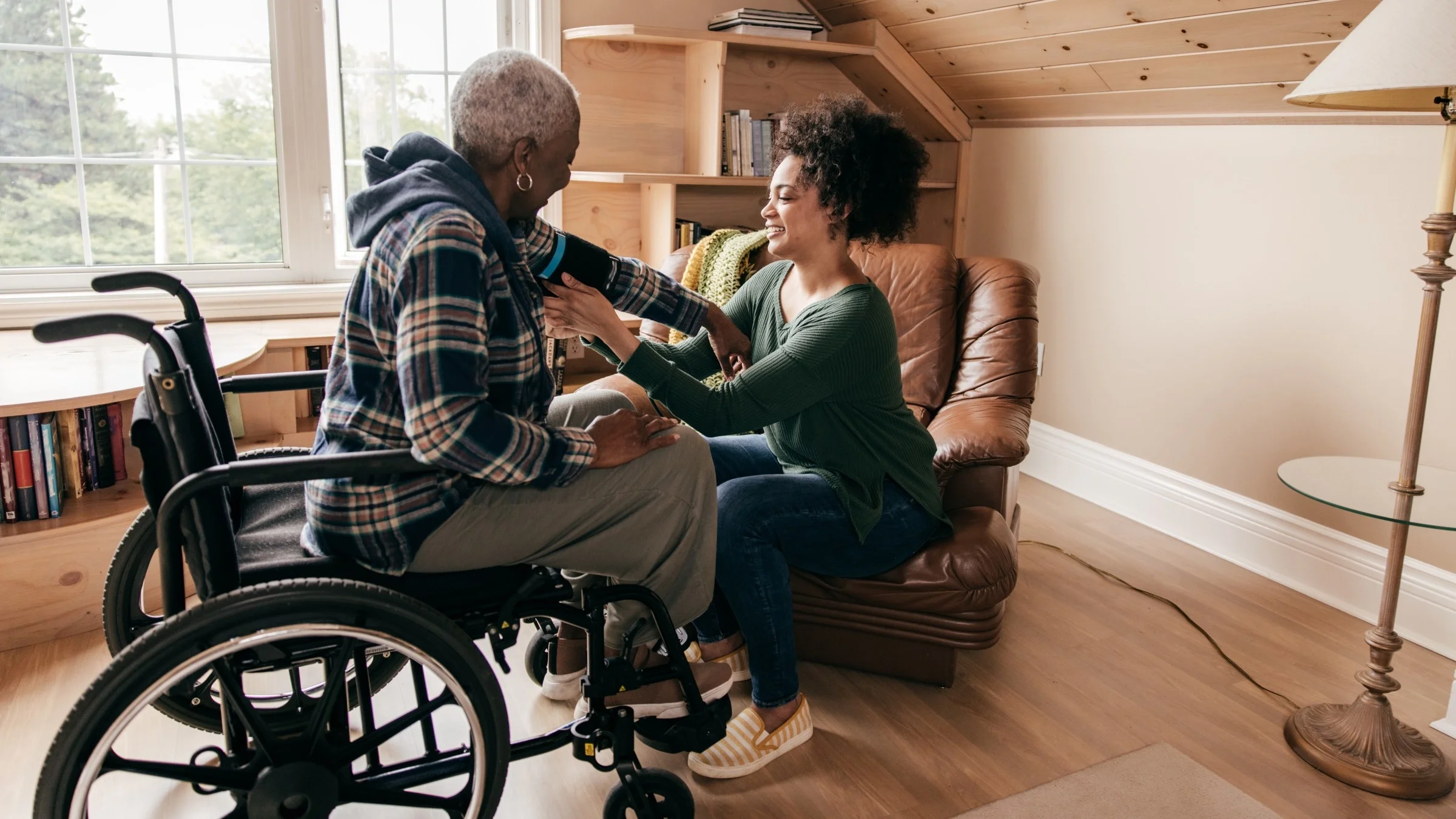 Young woman helping her grandmother take her blood pressure while in a wheel chair.