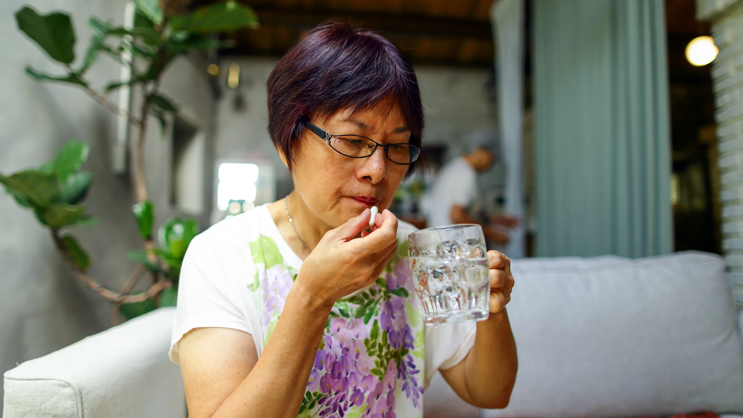 A woman takes her daily medication while holding a glass of water.