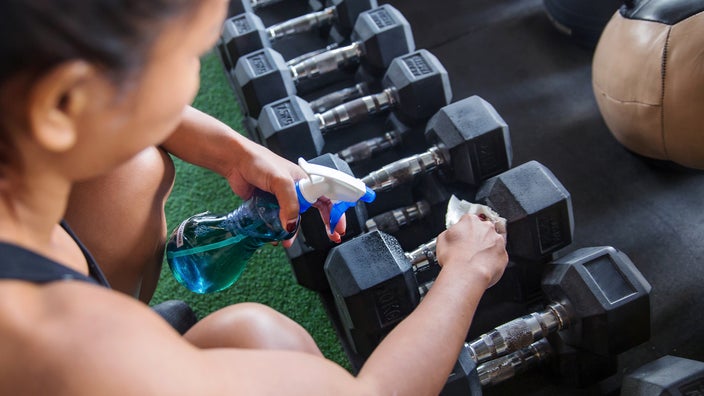 A woman cleans a dumbbell with disinfectant spray.