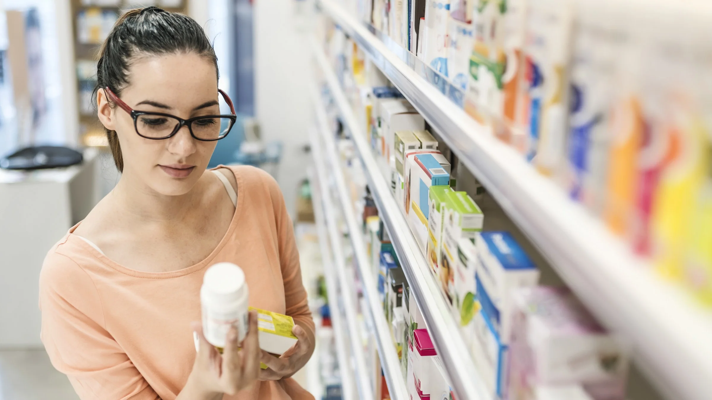 A person reading medication labels in a pharmacy aisle.