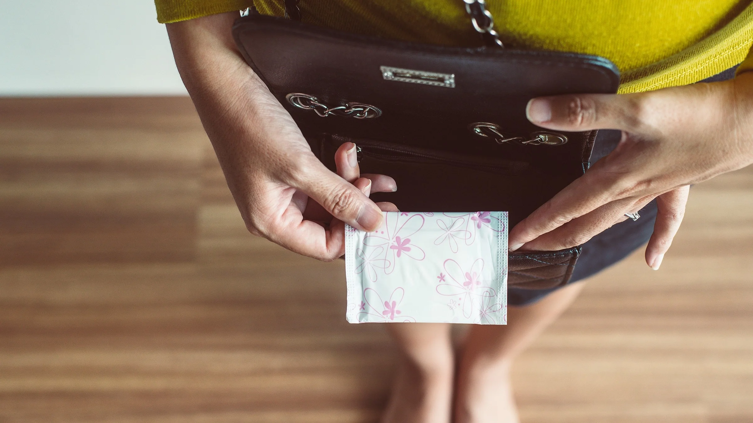 Overhead shot of a woman putting a period pad in her purse. You can see her feet below out of focus on the floor.