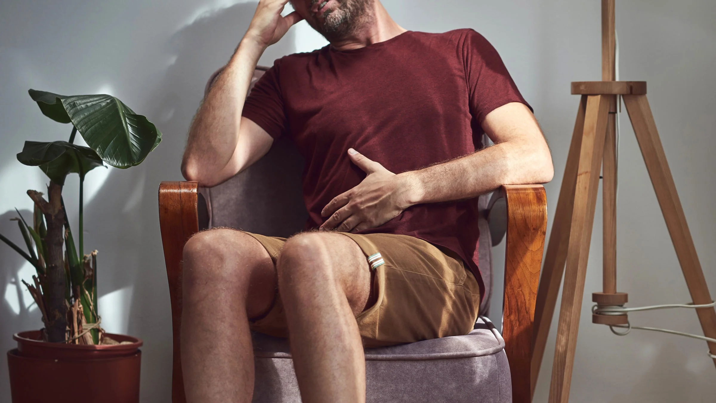 A man with stomach pain sits in a chair at home.