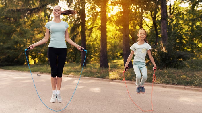 A smiling woman and girl jumping rope in a park.