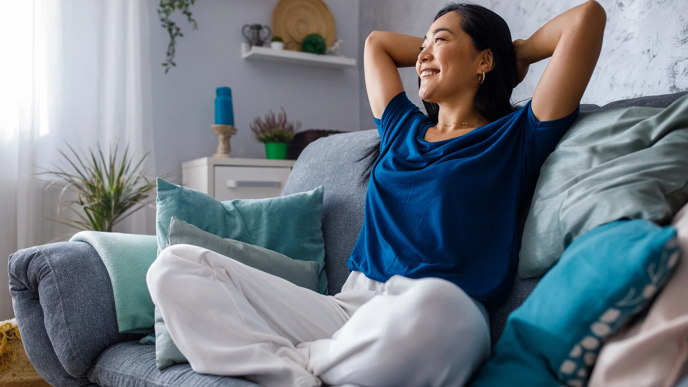 A woman is smiling and lounging on a sofa with her hands behind head.