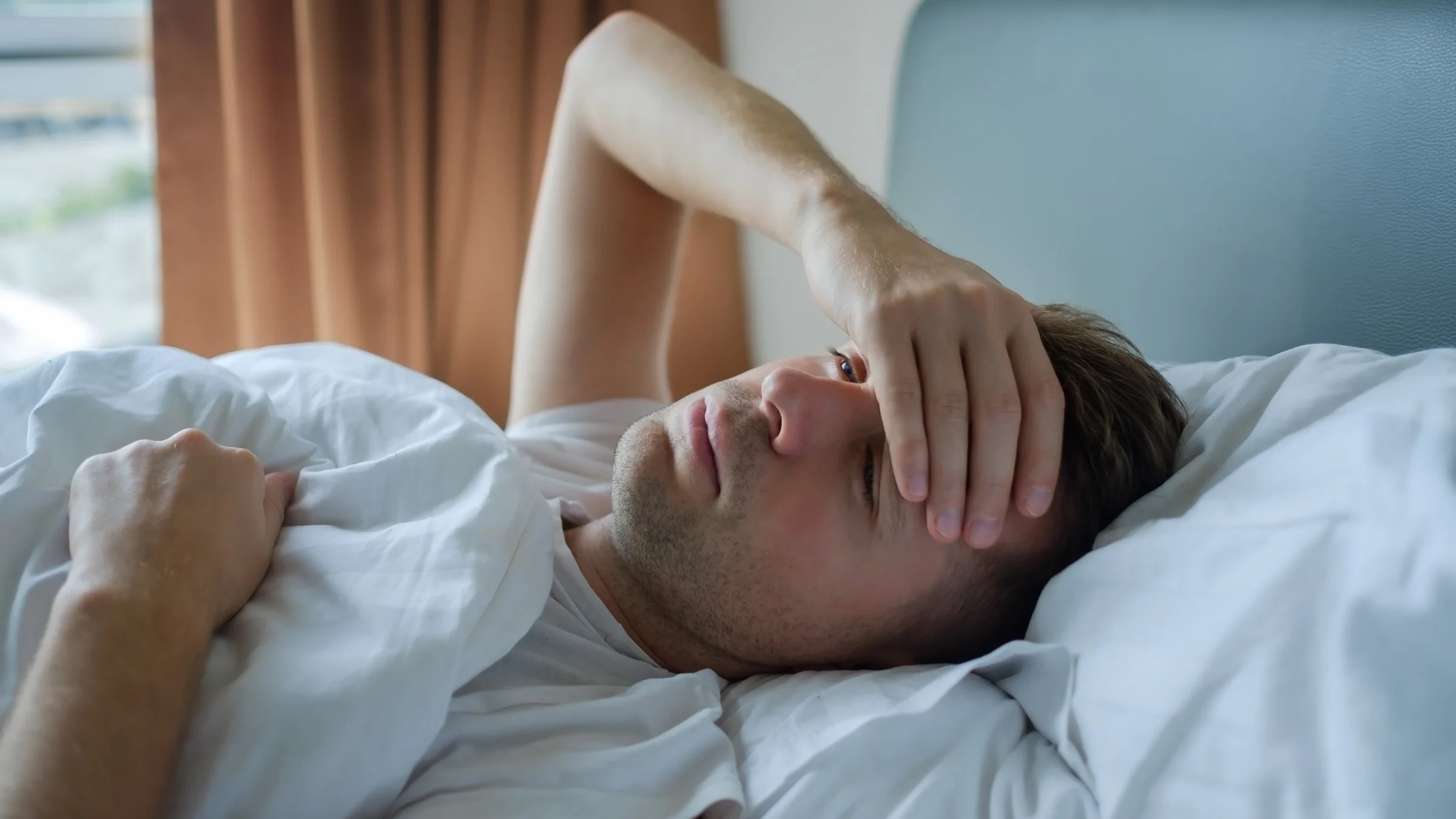 A man is awake in bed with his hand on his forehead.