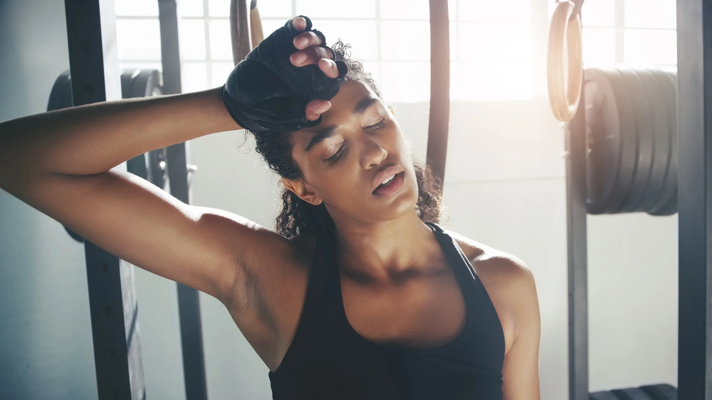 Young woman wiping sweat from her forehead after strength training exercises at the gym.