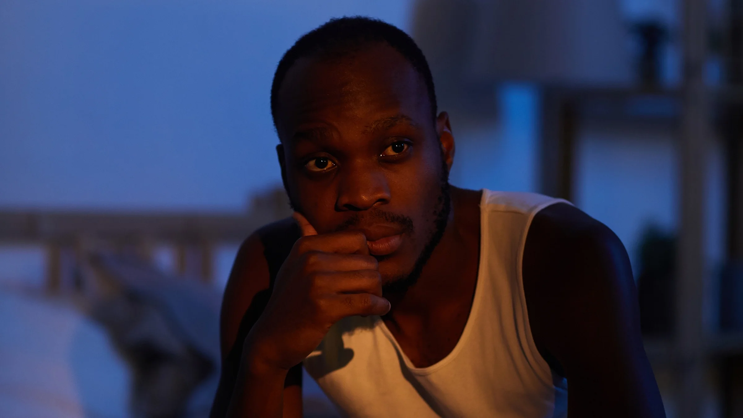Man sitting on the edge of his bed at night looking contemplative.