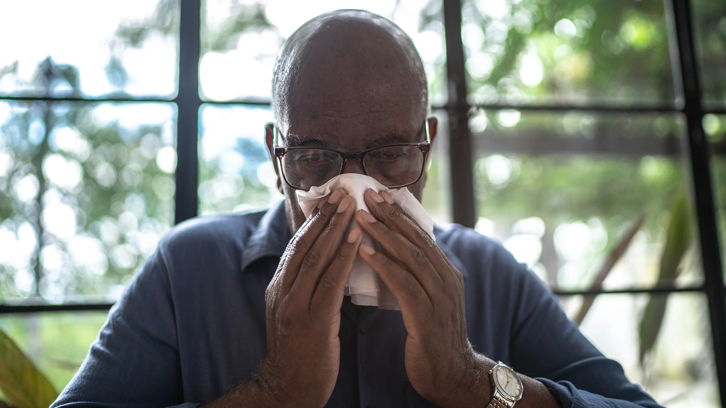 A man sneezes and wipes his nose with tissue paper.