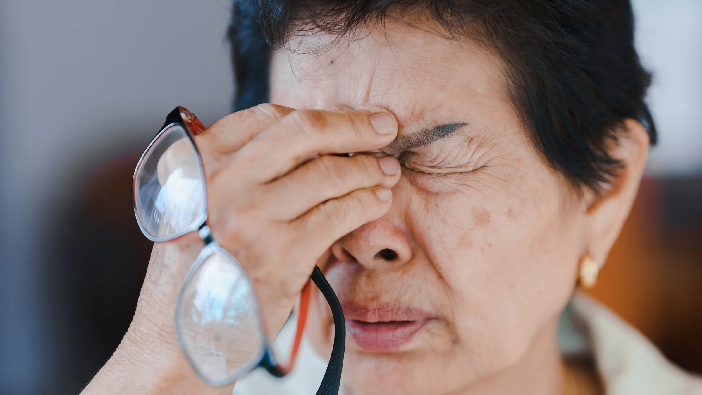 A person experiencing eye pain and taking their glasses off.