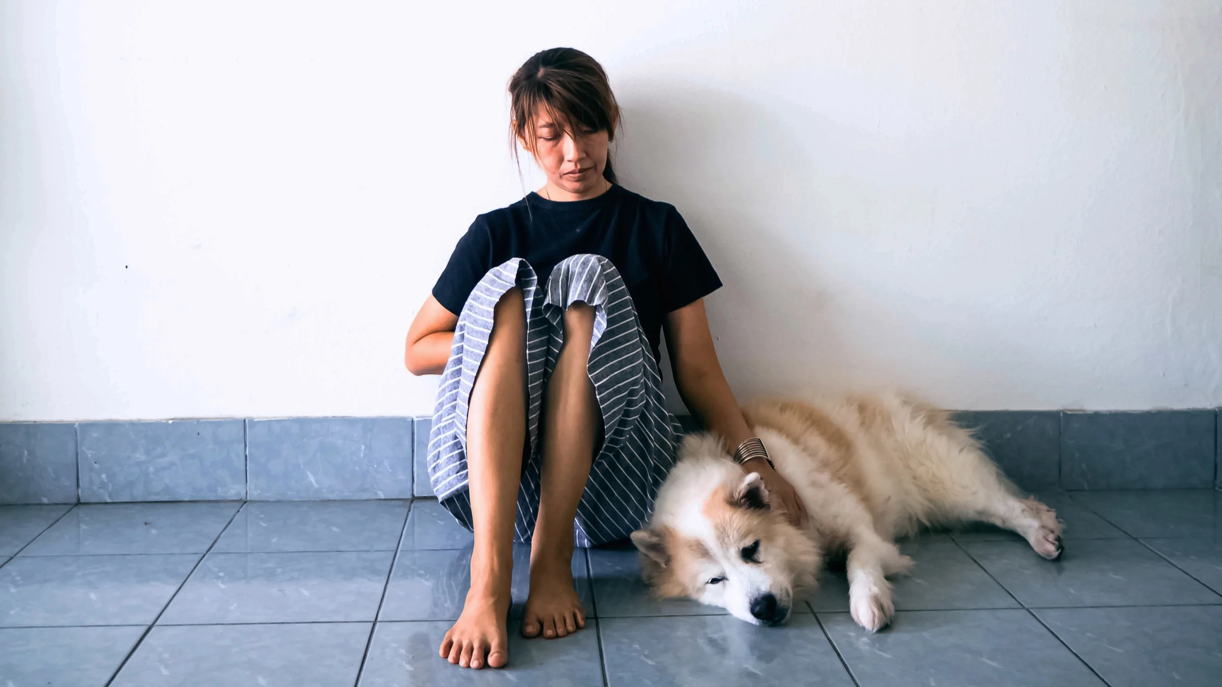 A sad person sitting on the ground with their dog.