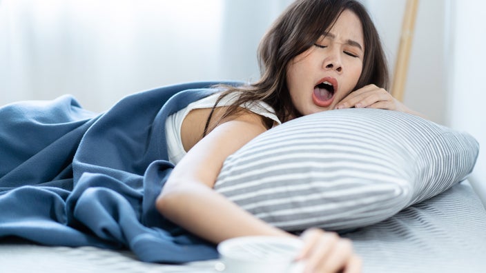 A person yawning and snoozing their alarm clock.