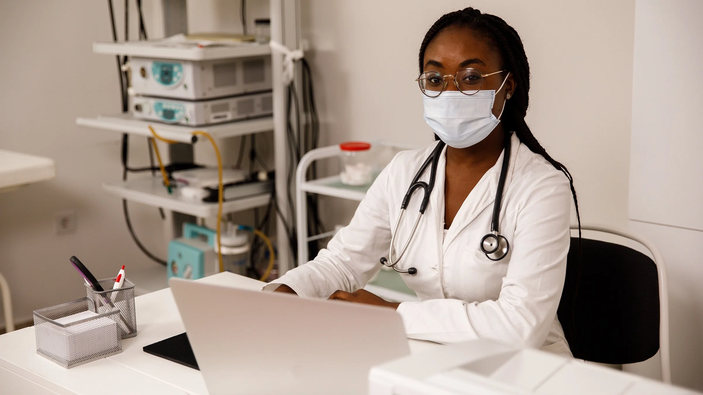 Young doctor sitting at her desk with medical equipment behind her.