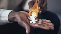 Close-up of a young woman taking white pills out of the pill bottle.
PeopleImages/E+ via Getty Images