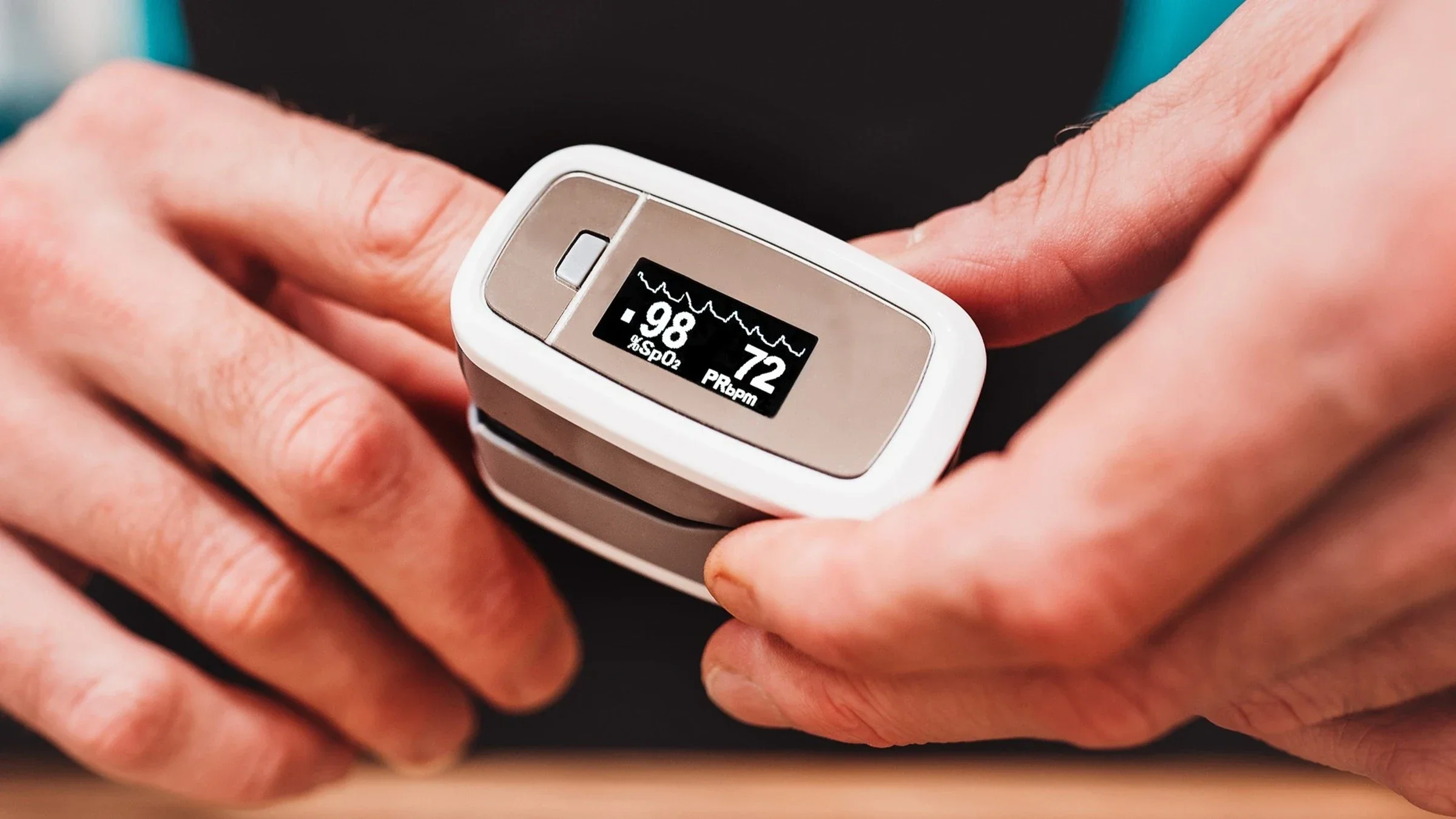 Close-up on someone using a Pulse Oximeter on their pointer finger. The digital display shows the numbers 98 and 72.
VanoVasaio via Shutterstock