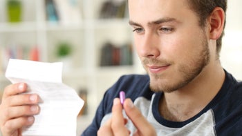 Atomoxetine: Interactions: closeup man holding purple pill reading prescription phamphlet  871176812
