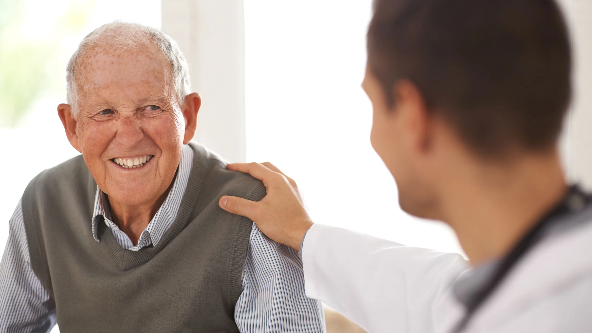 Senior man smiles at doctor during appointment.