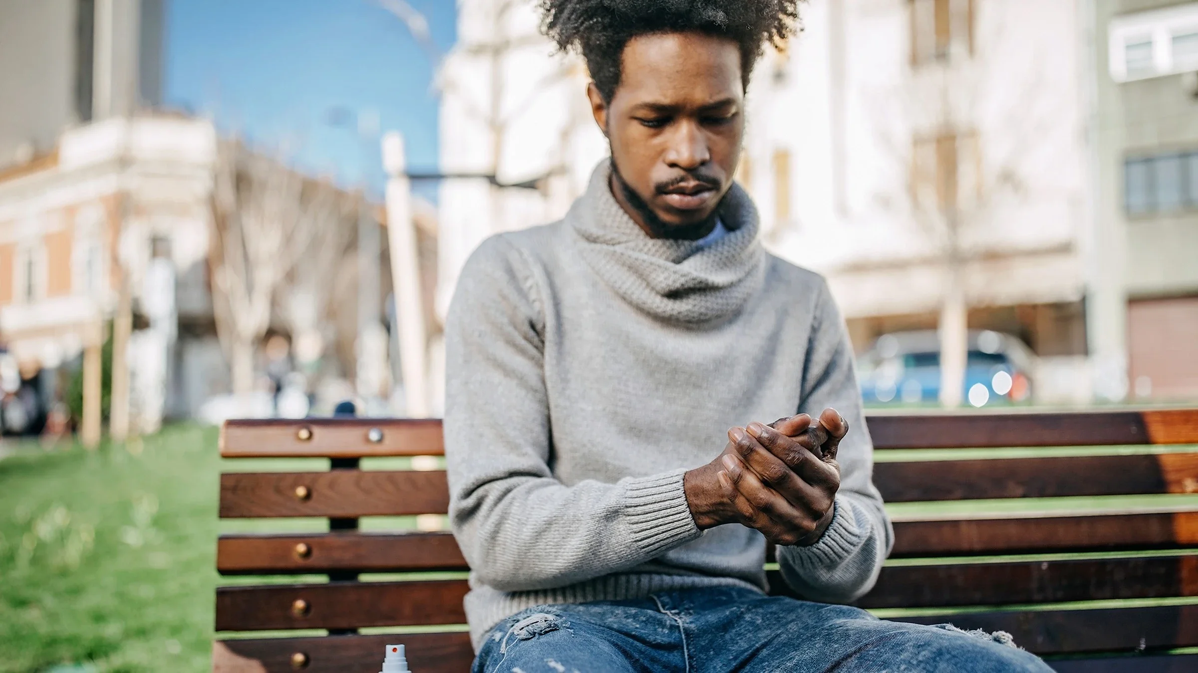 Black man on public wooden bench rubbing hands together with hand sanitizer