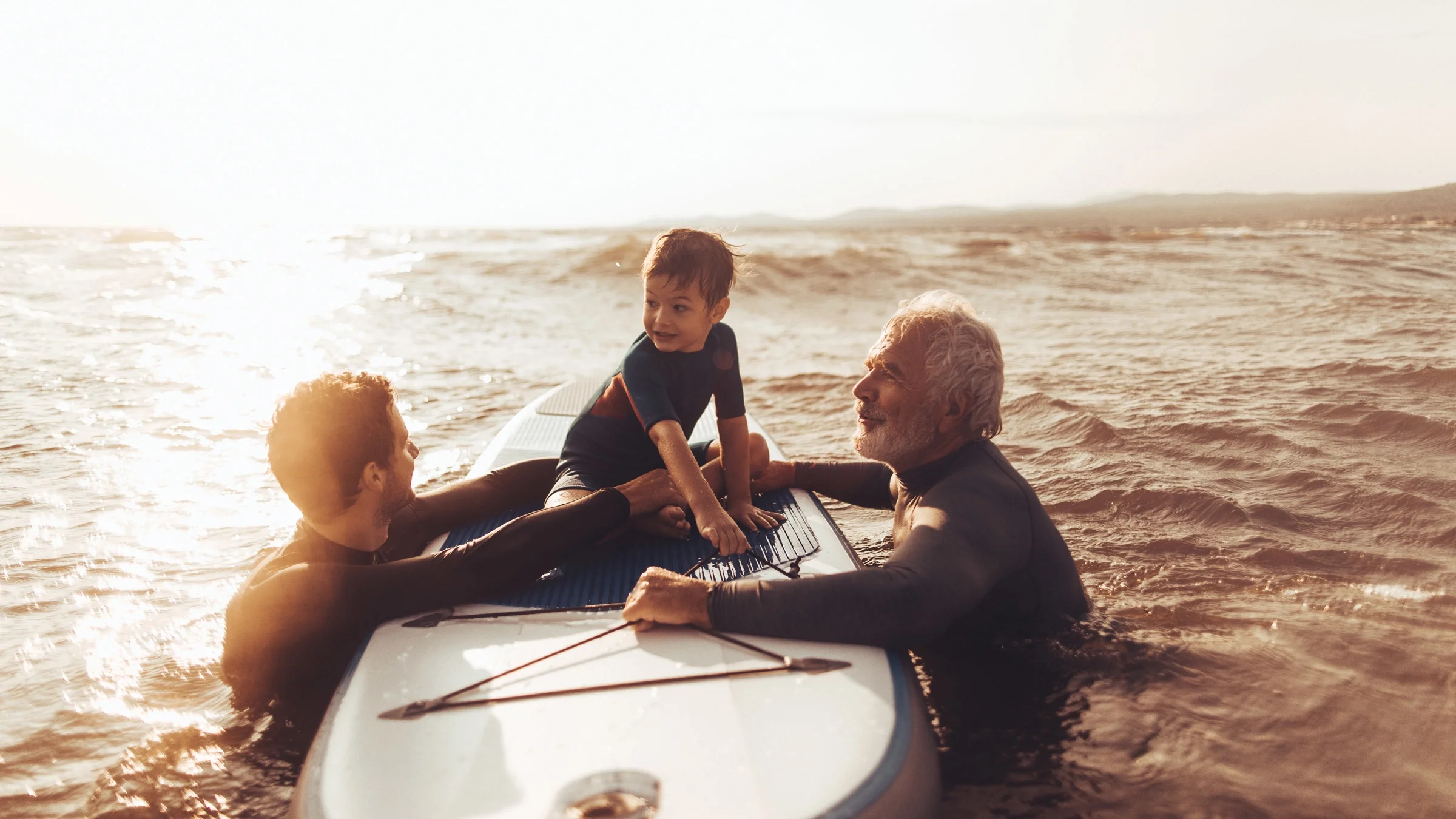 A little boy on a surfboard, with his dad and grandpa.