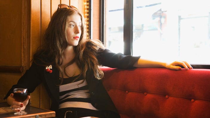 A person holding a glass of wine and looking out of a bar window.