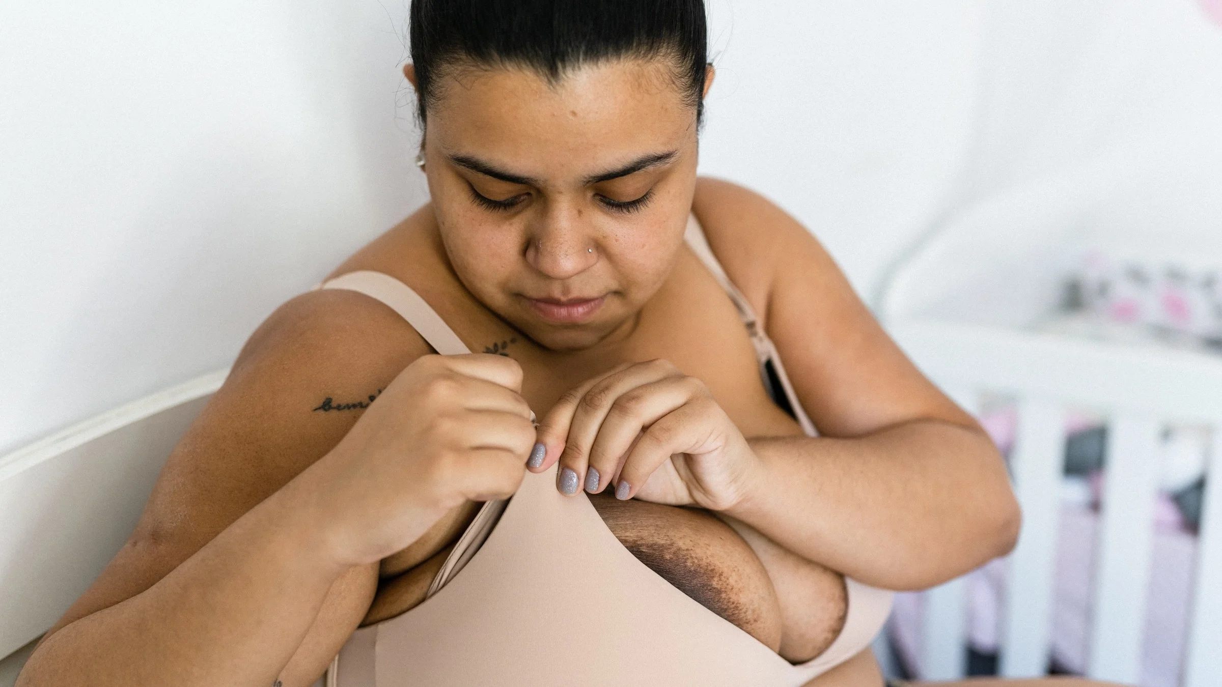 Woman closing the clasp of her breast feeding bra sitting in the baby's nursery.