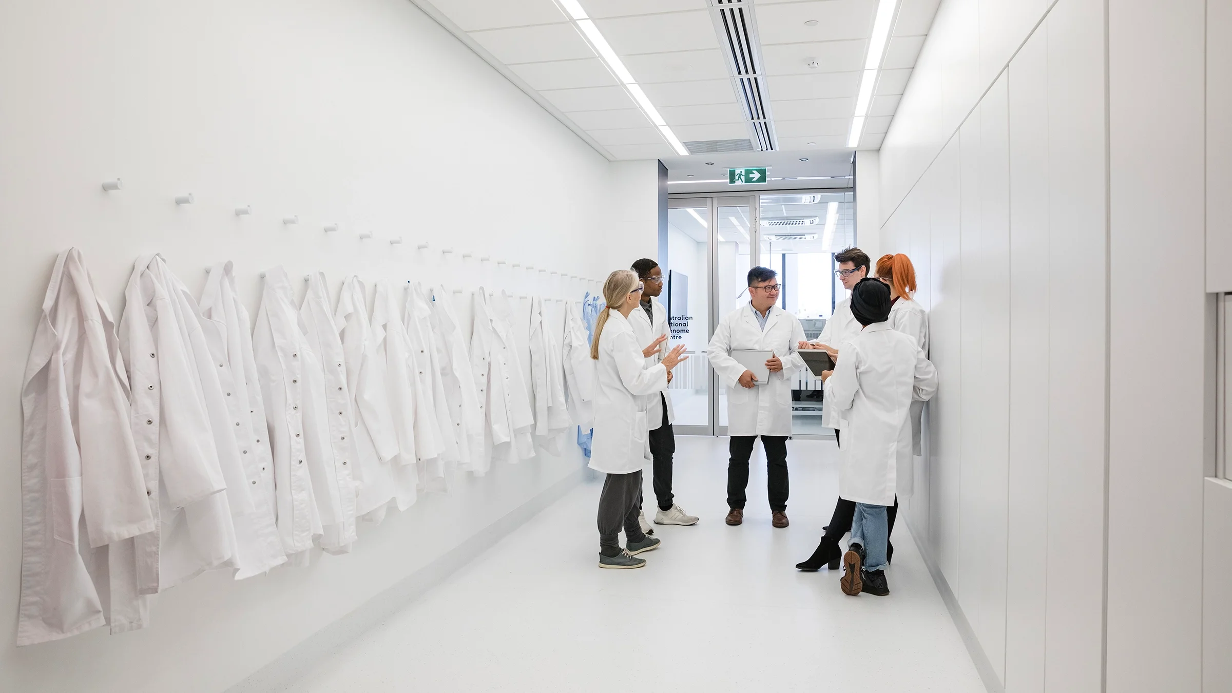 Doctors in white coats circled up, going over the schedule. They are standing in a very long, white hospital hallway.