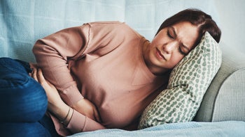 Ambien: young woman curled up on couch in stomach pain 1300136805