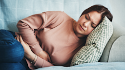 Young girl curled up on the couch in stomach pain.
PeopleImages/iStock via Getty Images
