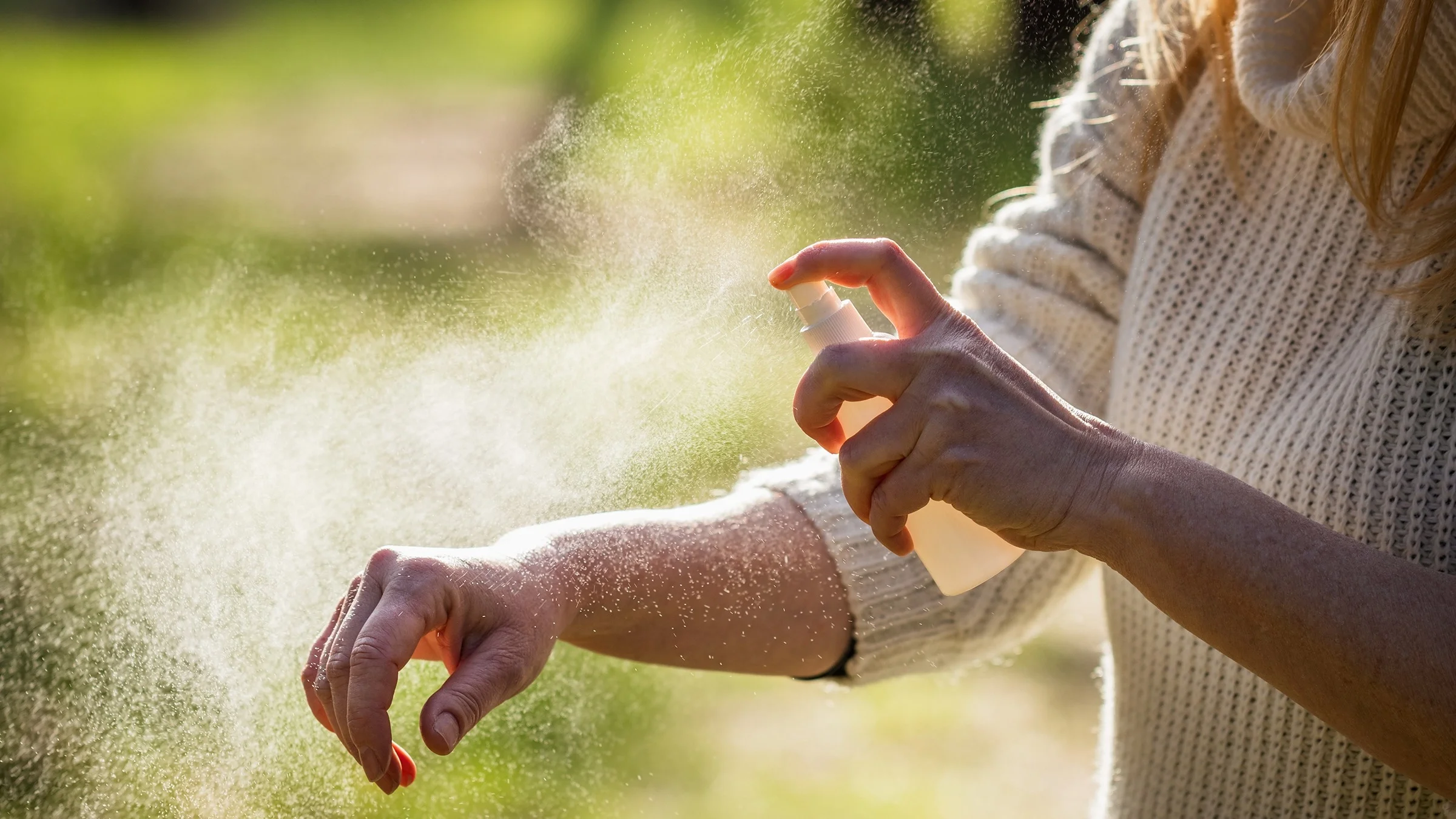 Close-up of a woman putting on bug spray with a spray bottle outside at a park.
