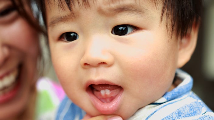 Close-up shot of a baby. The baby’s two bottom teeth are shown growing in.