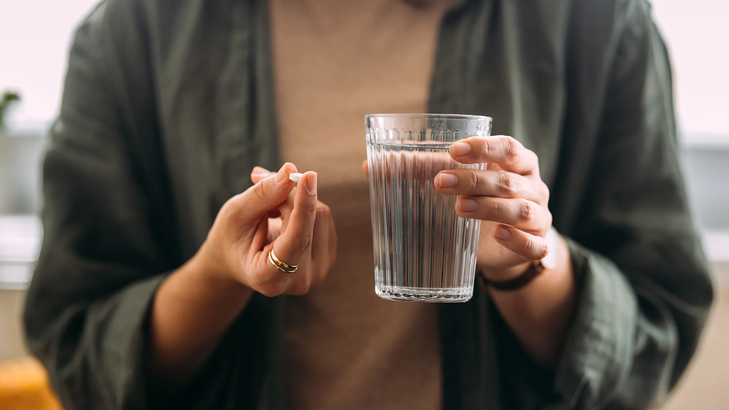 A person, in close-up, takes an oral medication with a glass of water.
FreshSplash/E+ via Getty Images