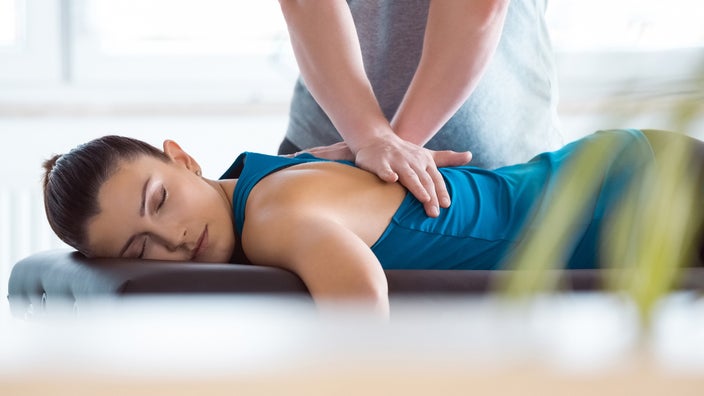 A physiotherapist massages and manipulates the muscles in a patient's upper back.