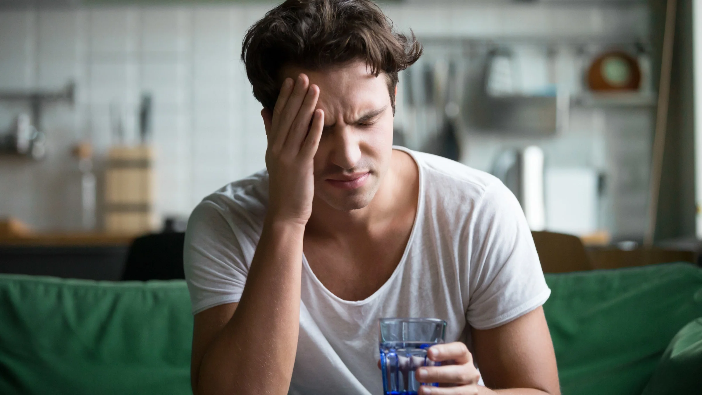 A person with a headache, drinking water on their couch.
