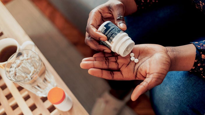 A woman pours three aspirin tablets into the palm of her hand.