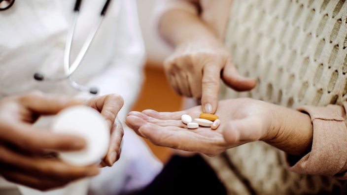 A person is pointing to medication in their hand while standing next to a healthcare provider.