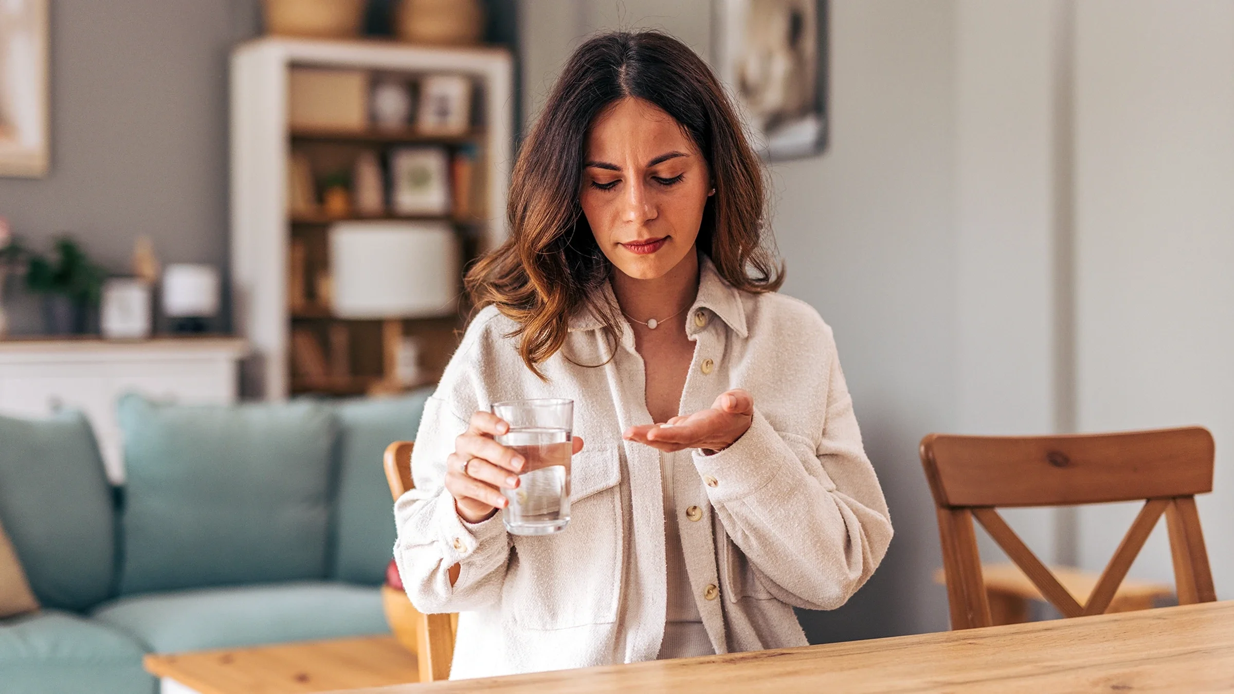 A woman prepares to take medicine at home with a glass of water.