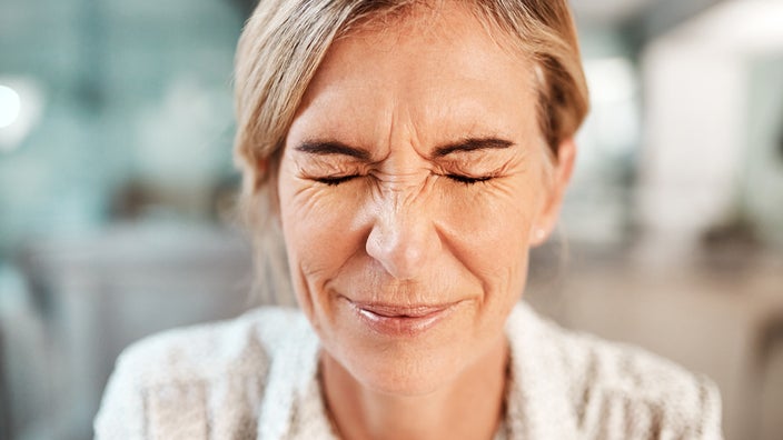 Close-up of a woman's face as she is wincing and closing her eyes.